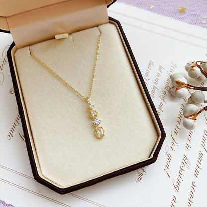 Necklace with geometric pendant displayed in a jewelry box, featuring sparkling stones on a gold chain.